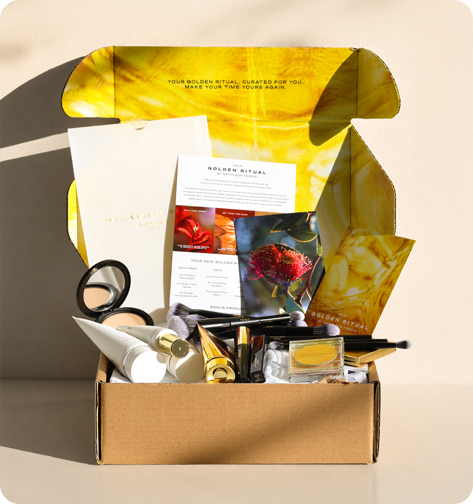 An open subscription beauty box filled with skincare and makeup items, including a mirror, cream tube, brushes, and a small jar, set against a warm beige background with a yellow printed insert.